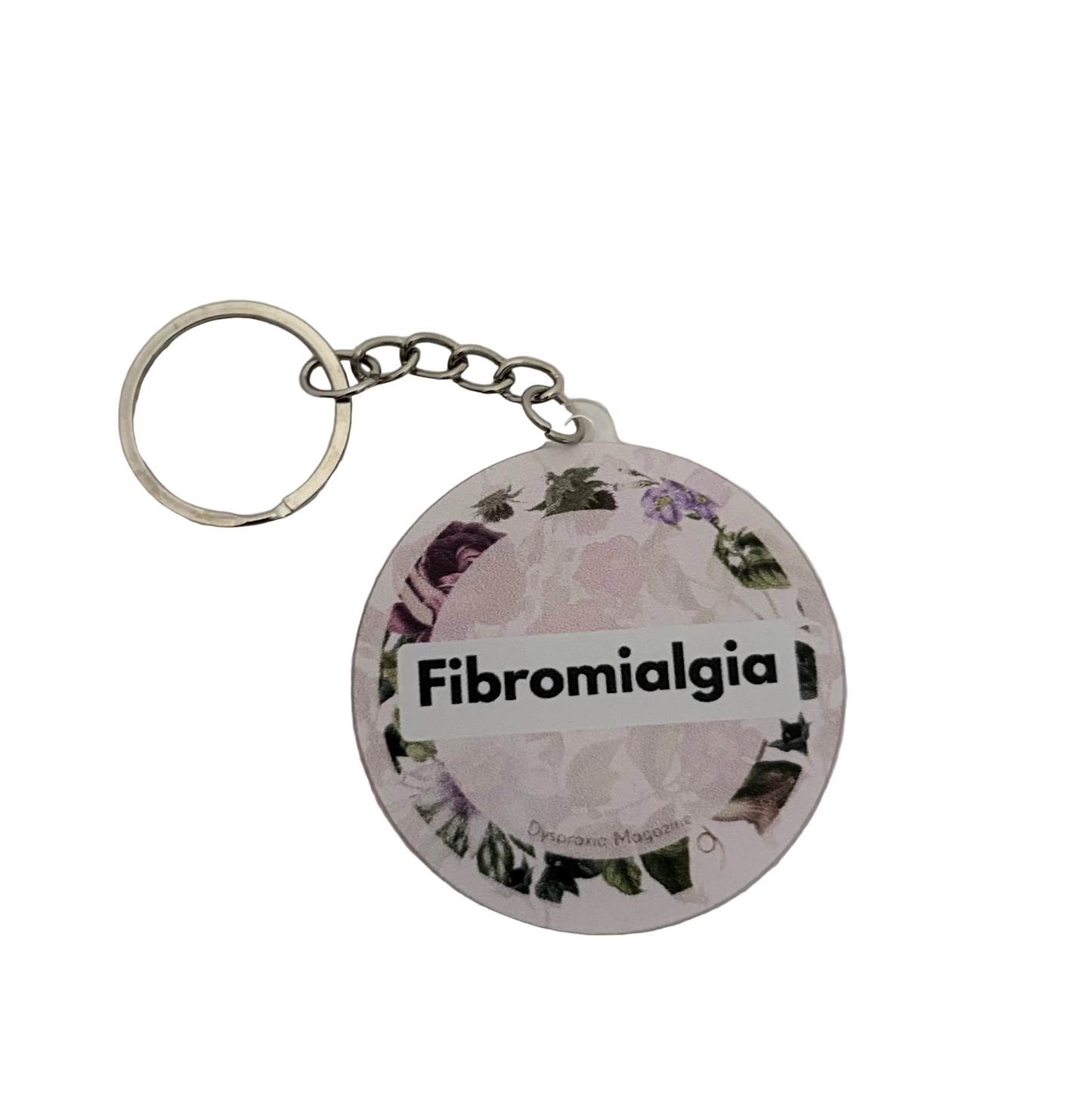 A round acrylic keychain featuring a floral design with the text 'Fibromialgia' printed across the center, attached to a silver metal split ring on a white textured background.
