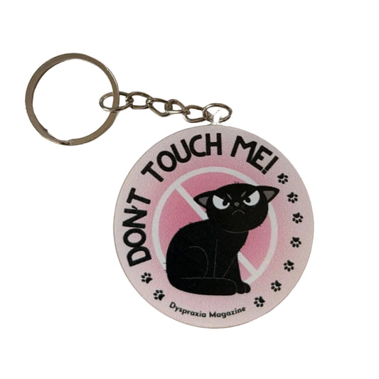 A round acrylic keychain featuring a black cat silhouette on a pink background with the text 'TOUCH ME! DON'T' and paw prints, attached to a silver metal key ring.
