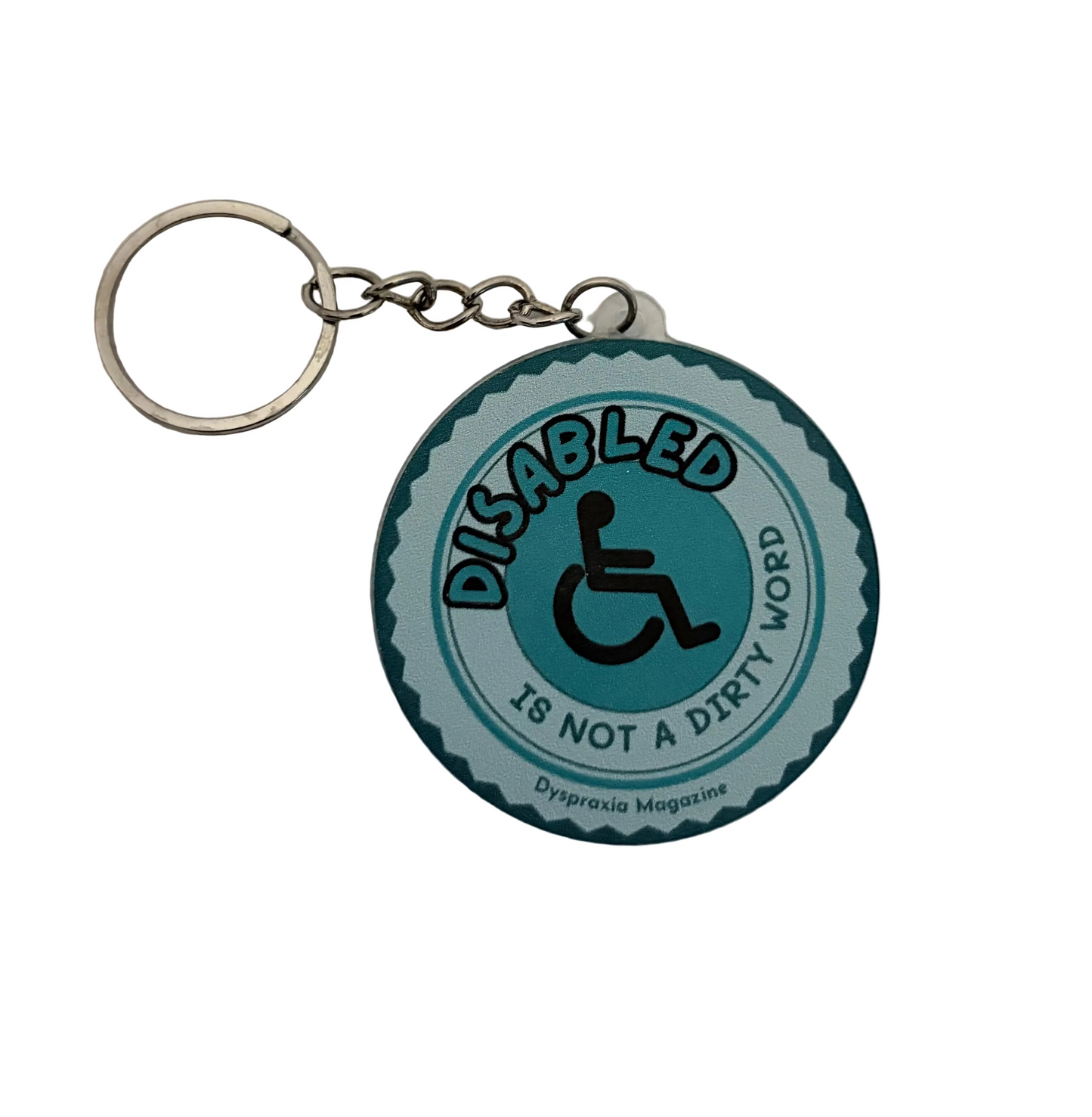 A circular metal keychain featuring a teal and black wheelchair symbol with the text 'DISABLED IS NOT A DIRTY WORD' and 'Dripraxia Magazine' printed on it, attached to a silver split key ring on a white textured background.