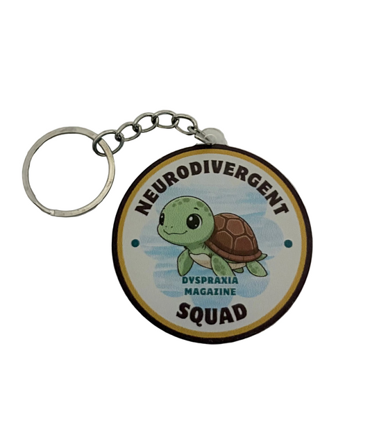 A round keychain featuring a cartoon green sea turtle on a light blue background, with the text 'NEURODIVERGENT SQUAD' at the bottom. The keychain has a silver metal split ring and chain, and is photographed on a white textured background.